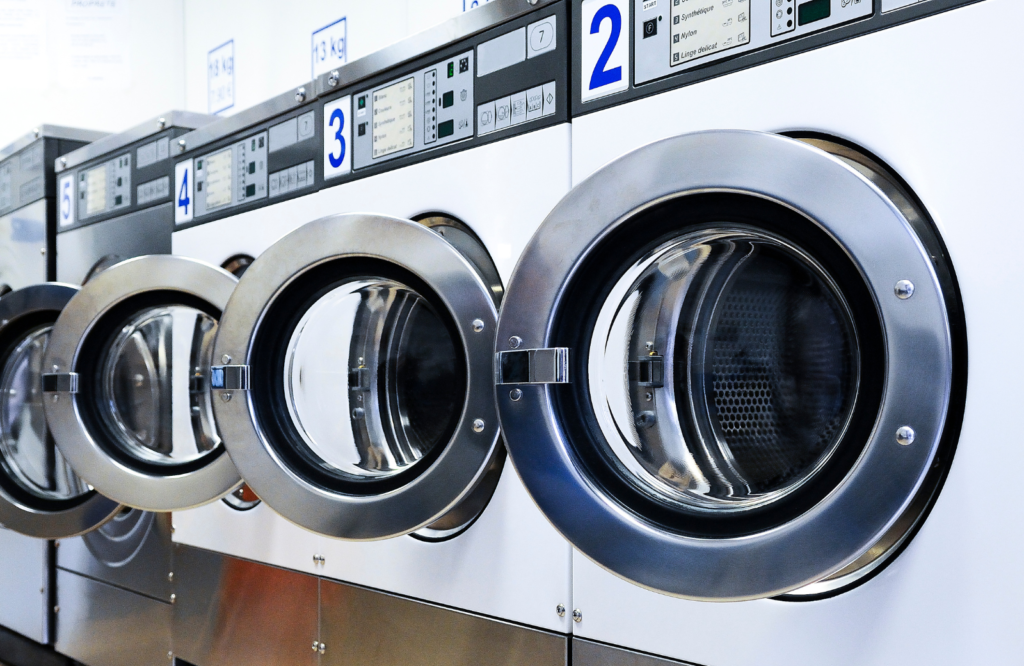 Front load commercial washing machines are shown lined up in a row. 